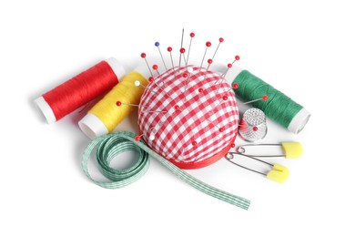 Checkered pincushion with sewing pins, spools of threads, ribbon and thimble isolated on white, above view