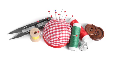 Checkered pincushion with sewing pins, spools of threads, thimble , cutter and buttons isolated on white, above view