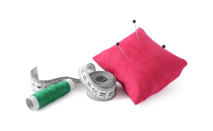 Photo of Pink pincushion with sewing pins, measuring tape and spool of thread isolated on white