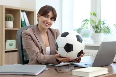 Smiling employee with soccer ball at table in office