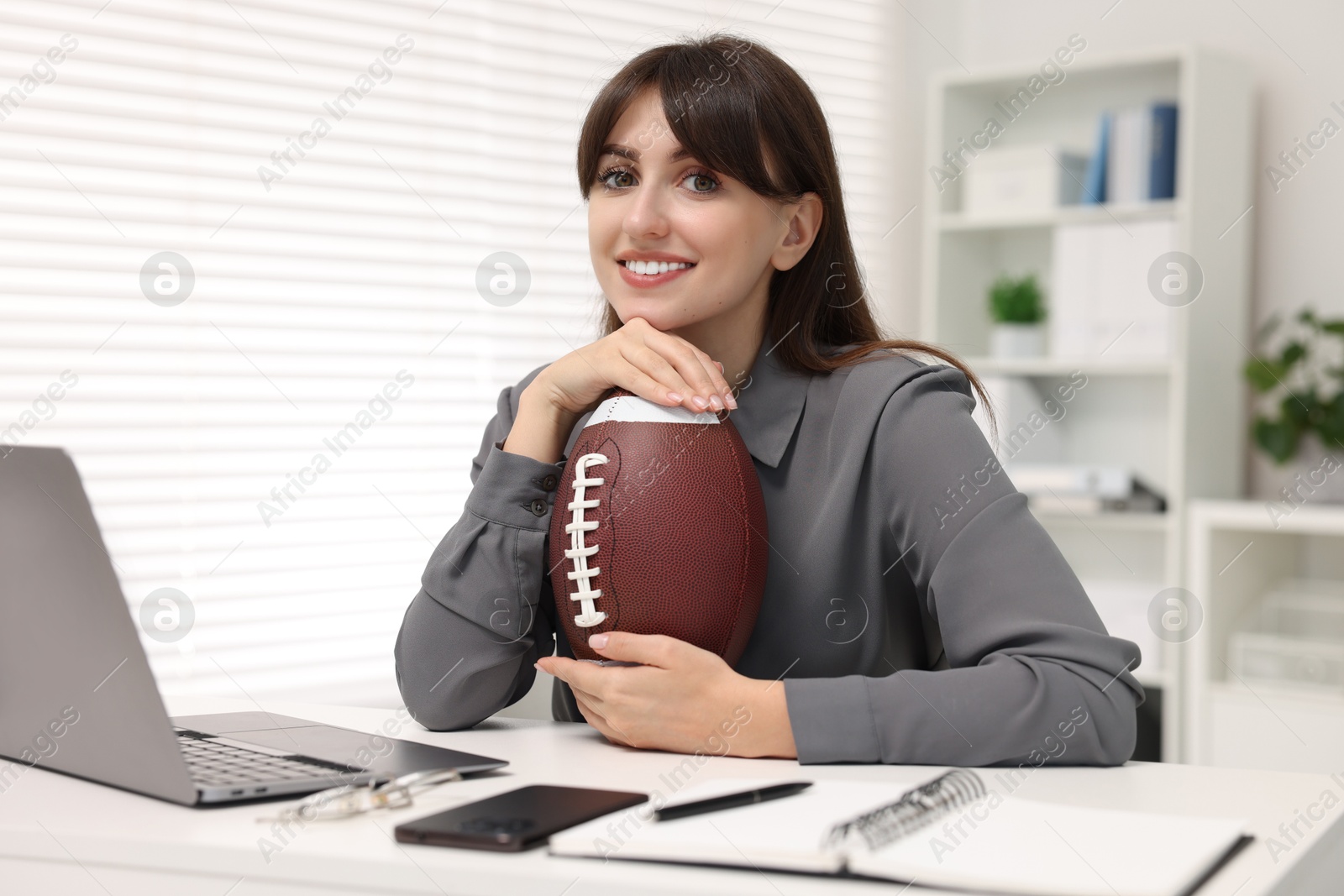 Photo of Smiling employee with american football ball at table in office