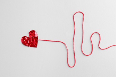 Red crumpled paper heart and thread on gray background, top view