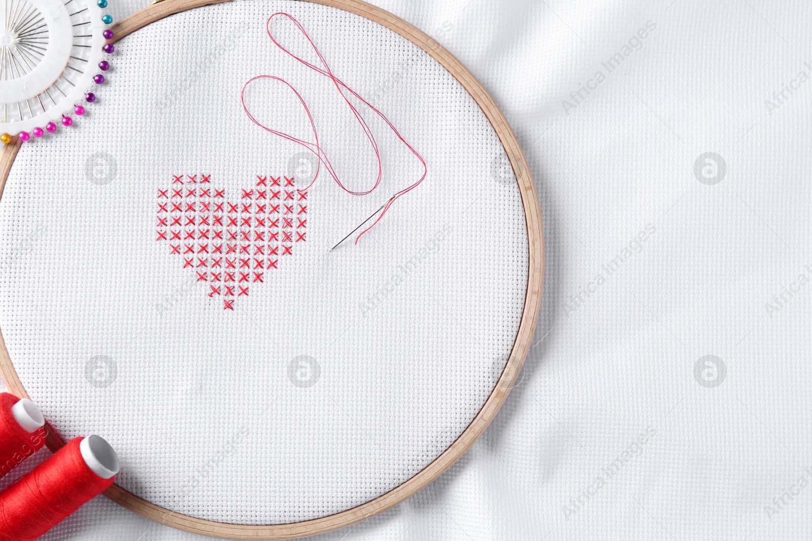 Photo of Embroidered red heart and needle on white cloth, top view. Space for text