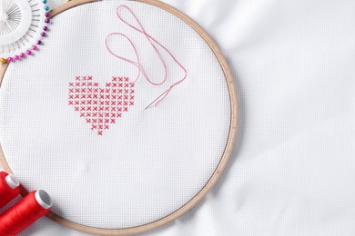 Embroidered red heart and needle on white cloth, top view. Space for text