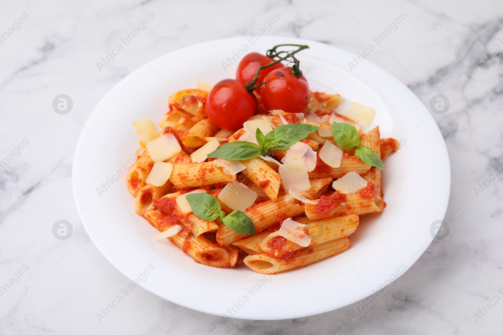 Photo of Tasty pasta with tomato sauce, cheese and basil on white marble table