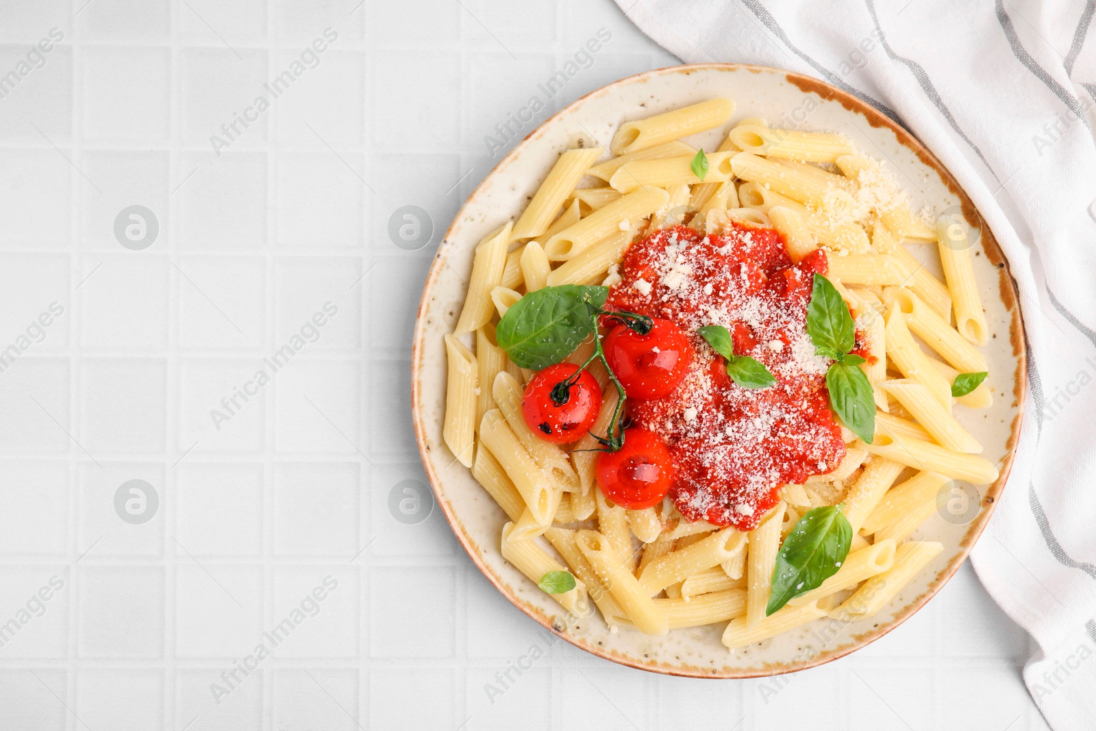 Photo of Tasty pasta with tomato sauce, cheese and basil on white tiled table, top view. Space for text