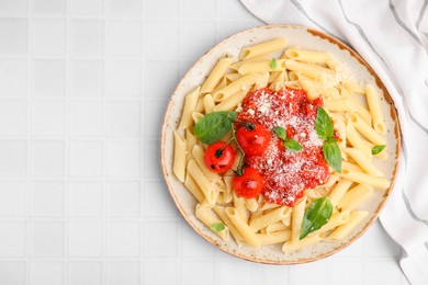 Tasty pasta with tomato sauce, cheese and basil on white tiled table, top view. Space for text