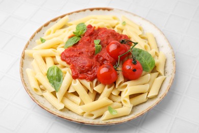 Tasty pasta with tomato sauce and basil on white tiled table