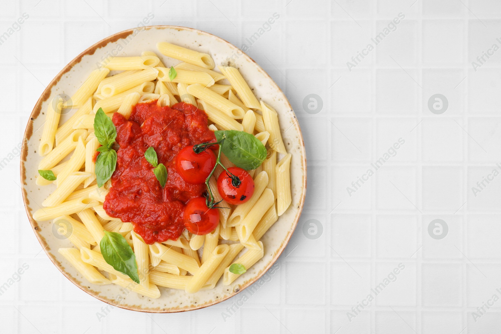 Photo of Tasty pasta with tomato sauce and basil on white tiled table, top view. Space for text