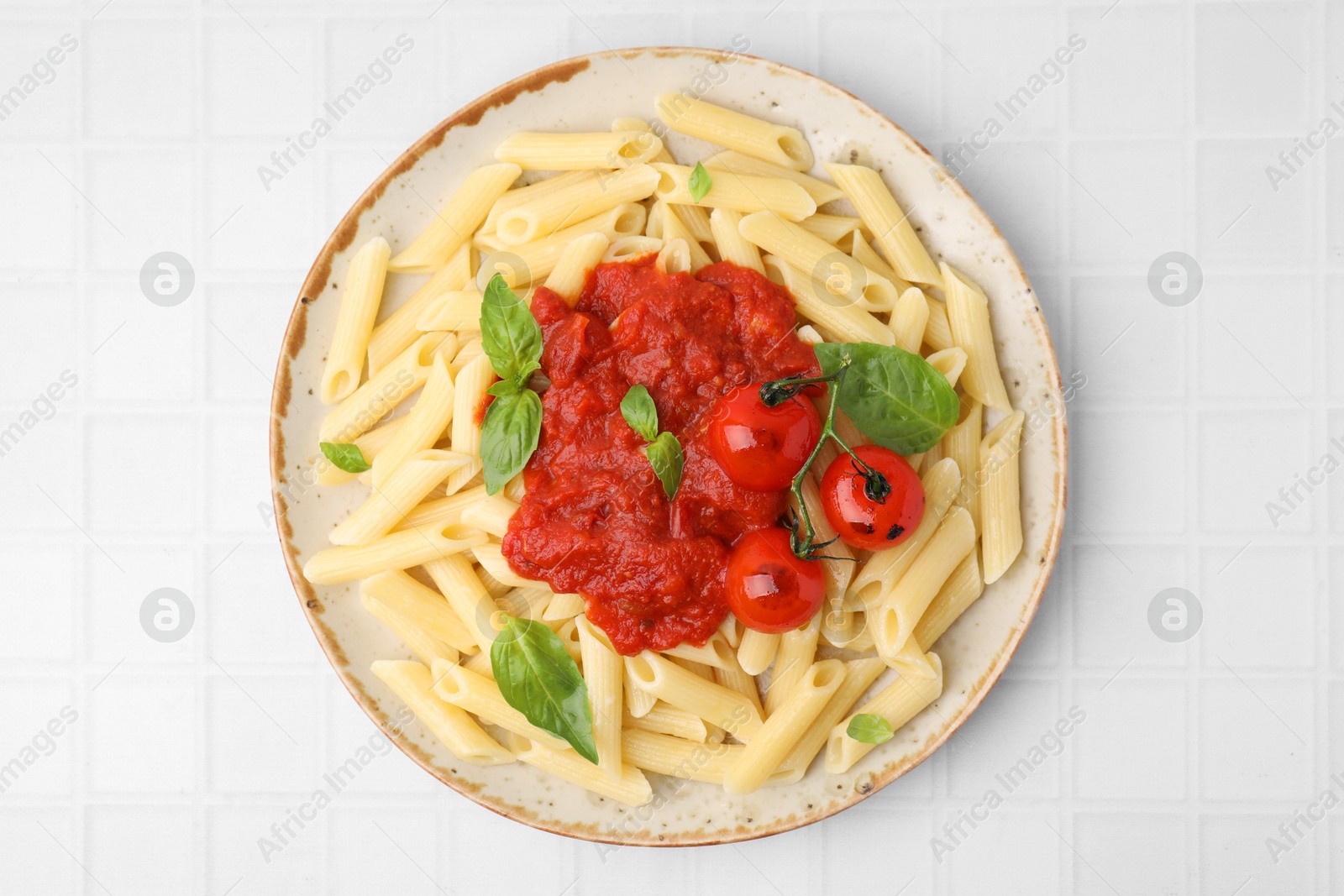 Photo of Tasty pasta with tomato sauce and basil on white tiled table, top view