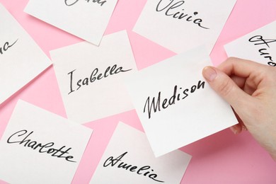 Photo of Woman holding paper stickers with name on pink background, closeup. Choosing baby's name