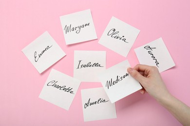 Woman holding paper stickers with name on pink background, top view. Choosing baby's name