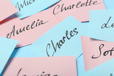 Paper stickers with different names on light blue background, closeup. Choosing baby's name