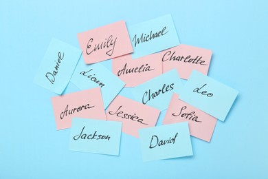 Paper stickers with different names on light blue background, top view. Choosing baby's name