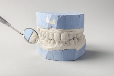 Dental model with gums and mouth mirror on gray background, closeup. Cast of teeth