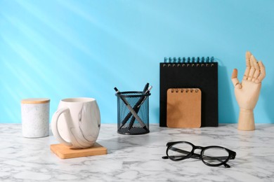 Photo of Stylish office workplace. Decor elements, glasses, cup and stationery on marble table near light blue wall