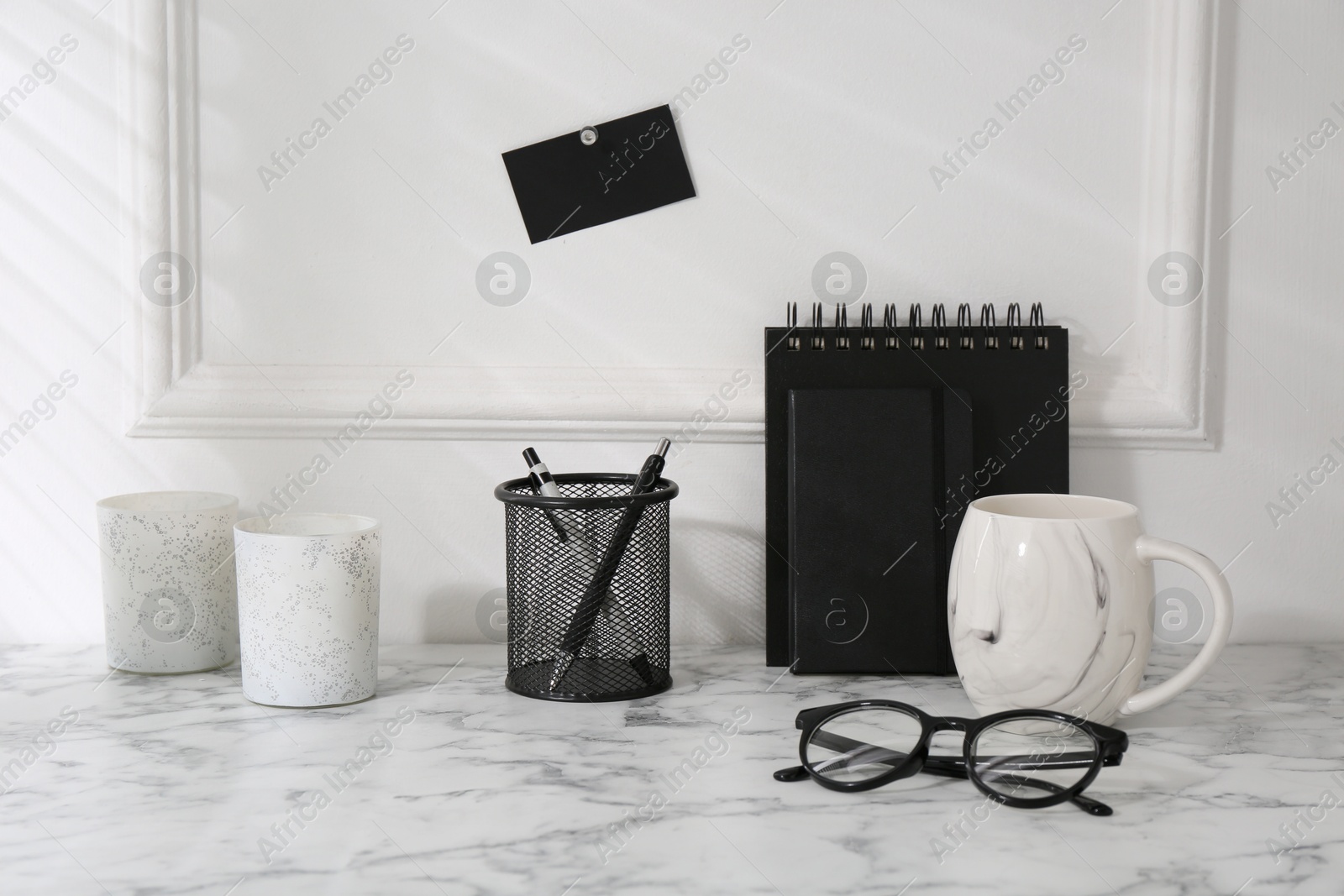 Photo of Stylish office workplace. Decor elements, glasses, cup and stationery on marble table near white wall