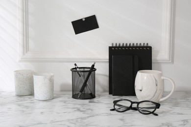 Photo of Stylish office workplace. Decor elements, glasses, cup and stationery on marble table near white wall