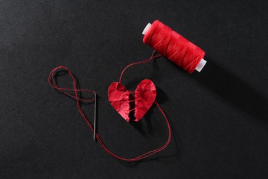 Halves of torn paper heart connected by thread on black background, flat lay. Relationship problem concept