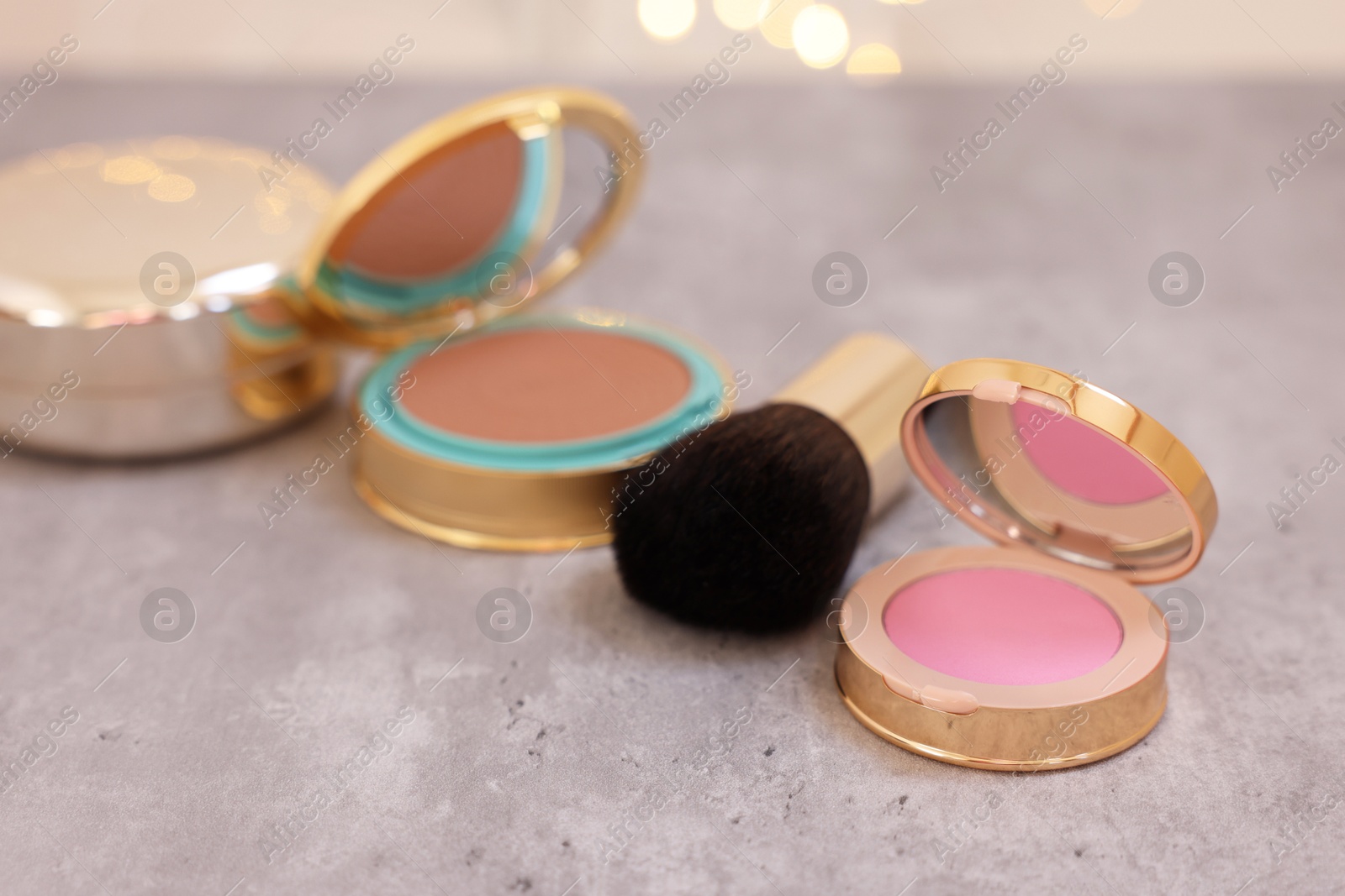 Photo of Face blusher and other cosmetic products on grey textured table, closeup