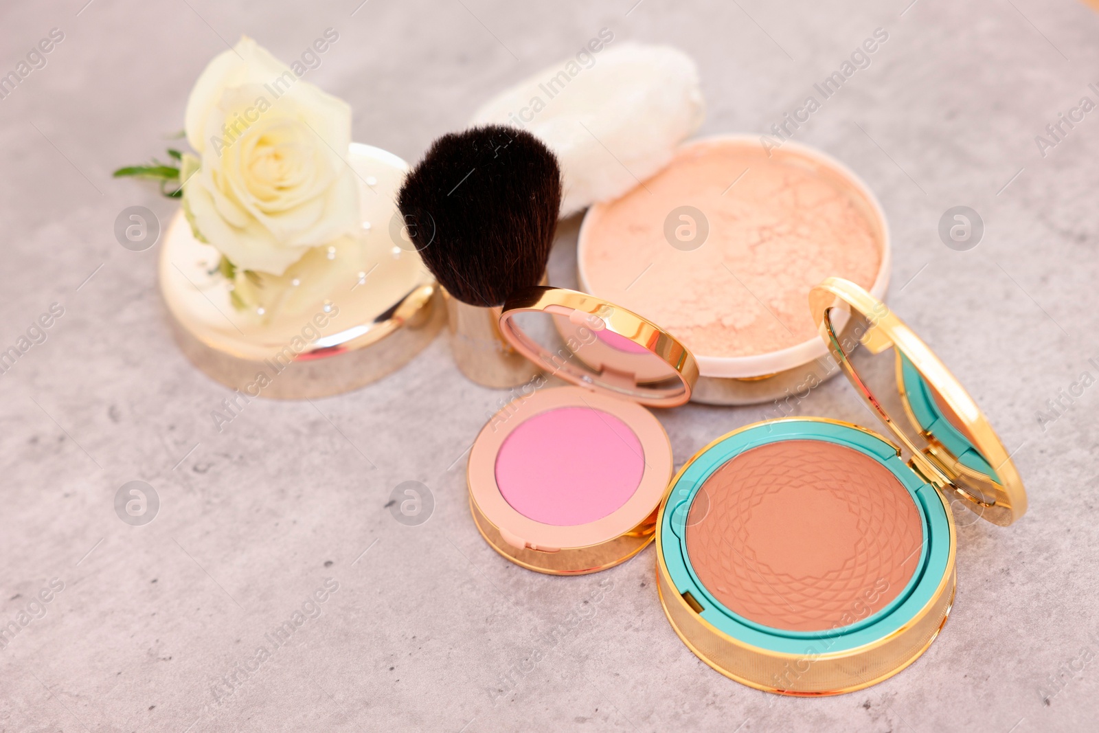 Photo of Bronzer, powder, blusher, brush and rose flower on grey textured table, above view