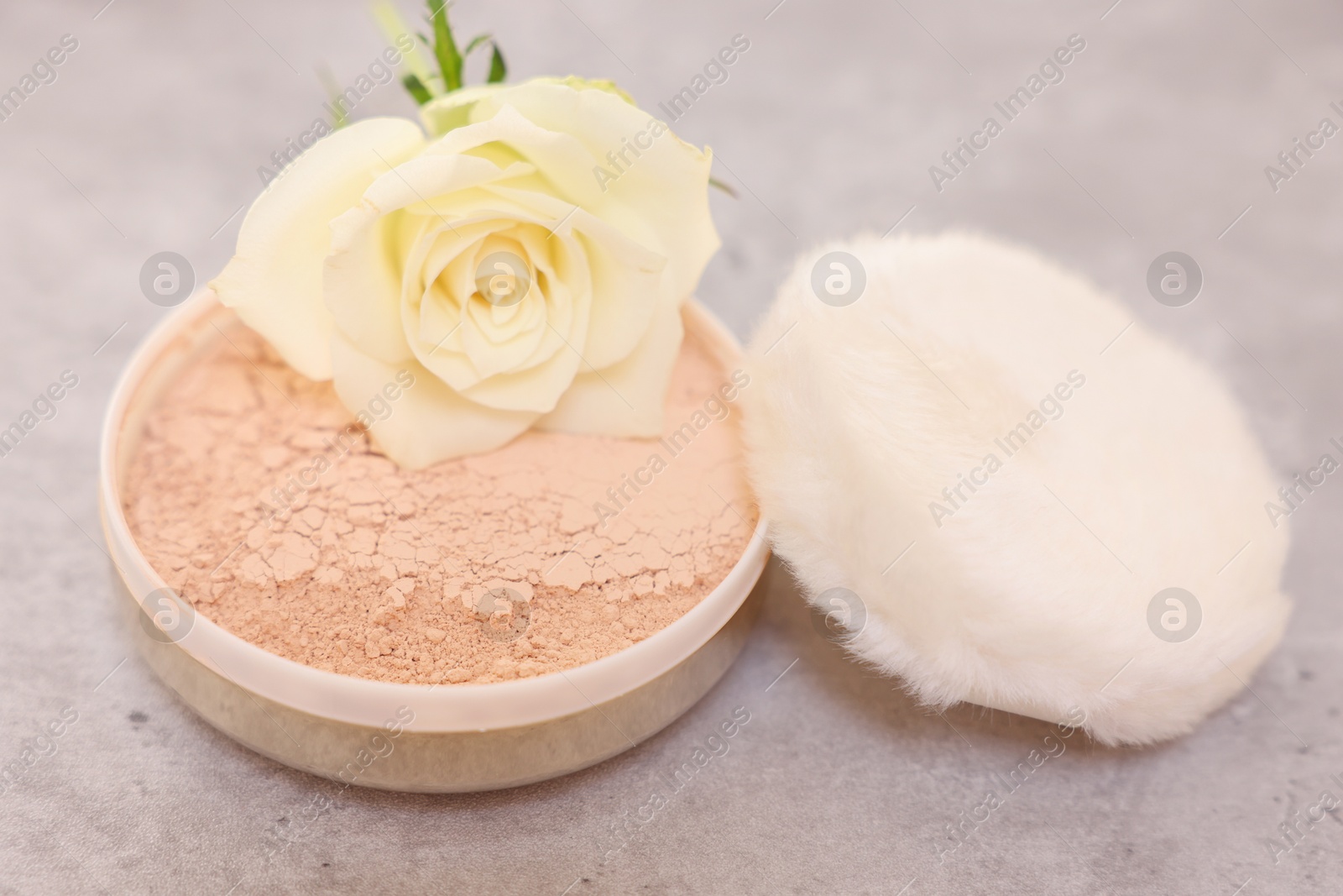 Photo of Face powder, puff applicator and rose flower on grey textured table, closeup