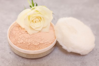 Face powder, puff applicator and rose flower on grey textured table, closeup