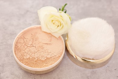 Photo of Face powder, puff applicator and rose flower on grey textured table, closeup