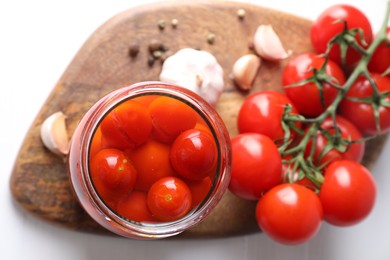 Tasty pickled tomatoes in jar, fresh vegetables and spices on white table, top view