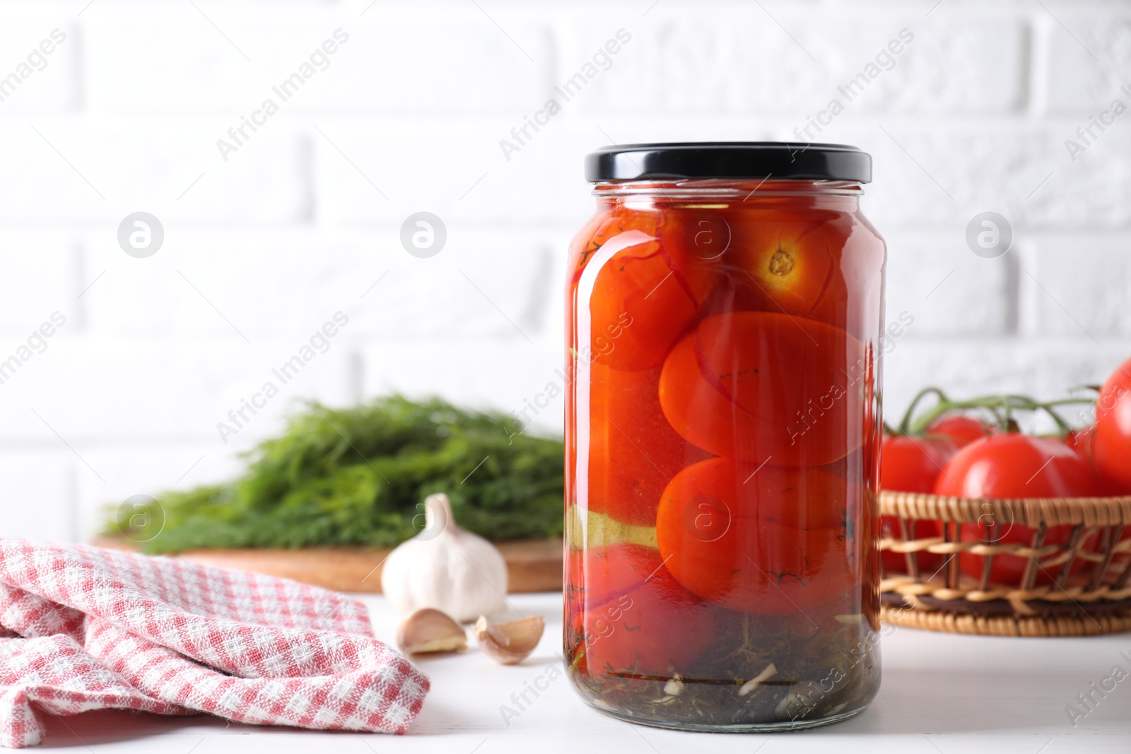 Photo of Tasty pickled tomatoes in jar and garlic on white table
