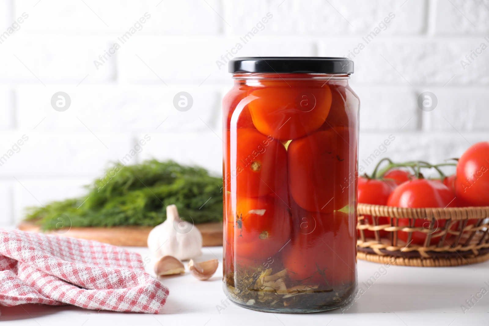 Photo of Tasty pickled tomatoes in jar and garlic on white table