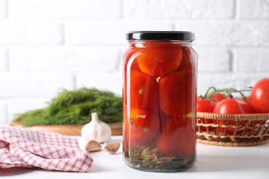 Photo of Tasty pickled tomatoes in jar and garlic on white table