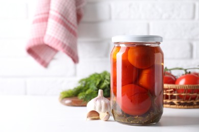 Photo of Tasty pickled tomatoes in jar and garlic on white table, space for text