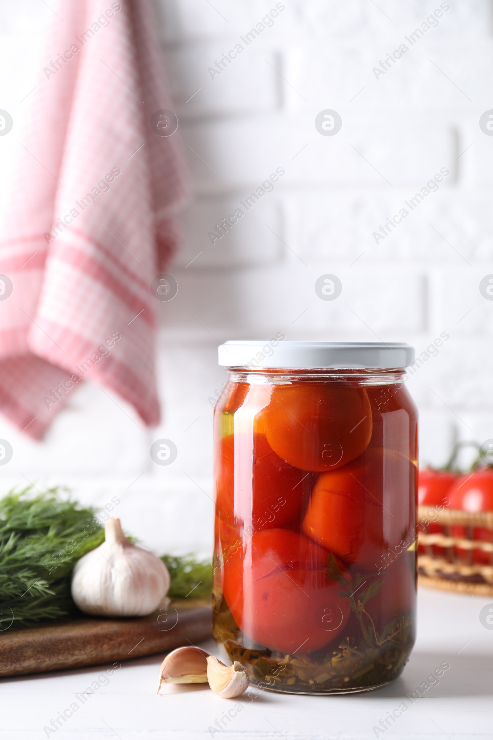 Photo of Tasty pickled tomatoes in jar, garlic and dill on white table