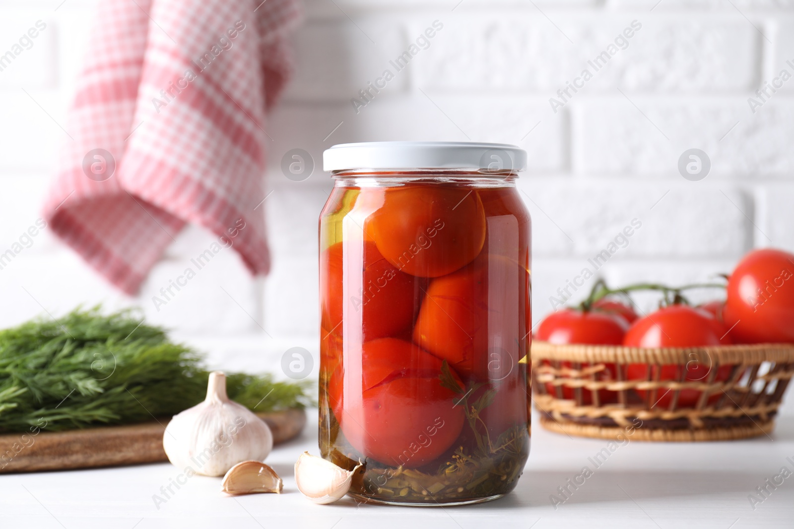 Photo of Tasty pickled tomatoes in jar, garlic and dill on white table