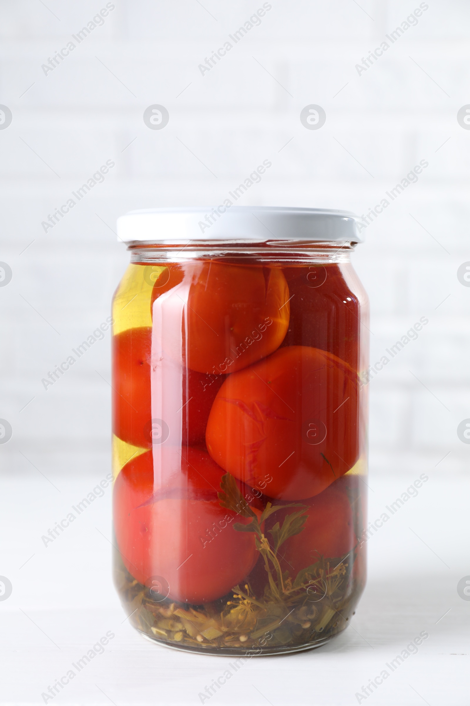 Photo of Tasty pickled tomatoes in jar on white table
