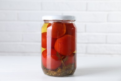 Photo of Tasty pickled tomatoes in jar on white table