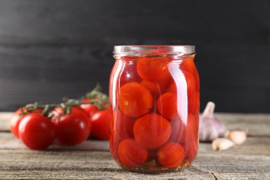 Photo of Tasty pickled tomatoes in jar, fresh vegetables and garlic on wooden table