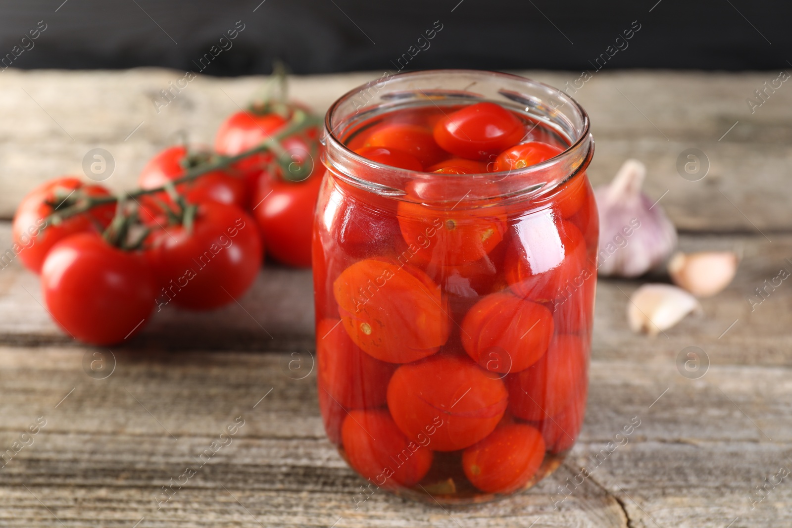 Photo of Tasty pickled tomatoes in jar, fresh vegetables and garlic on wooden table