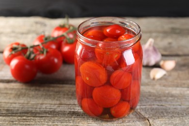 Tasty pickled tomatoes in jar, fresh vegetables and garlic on wooden table