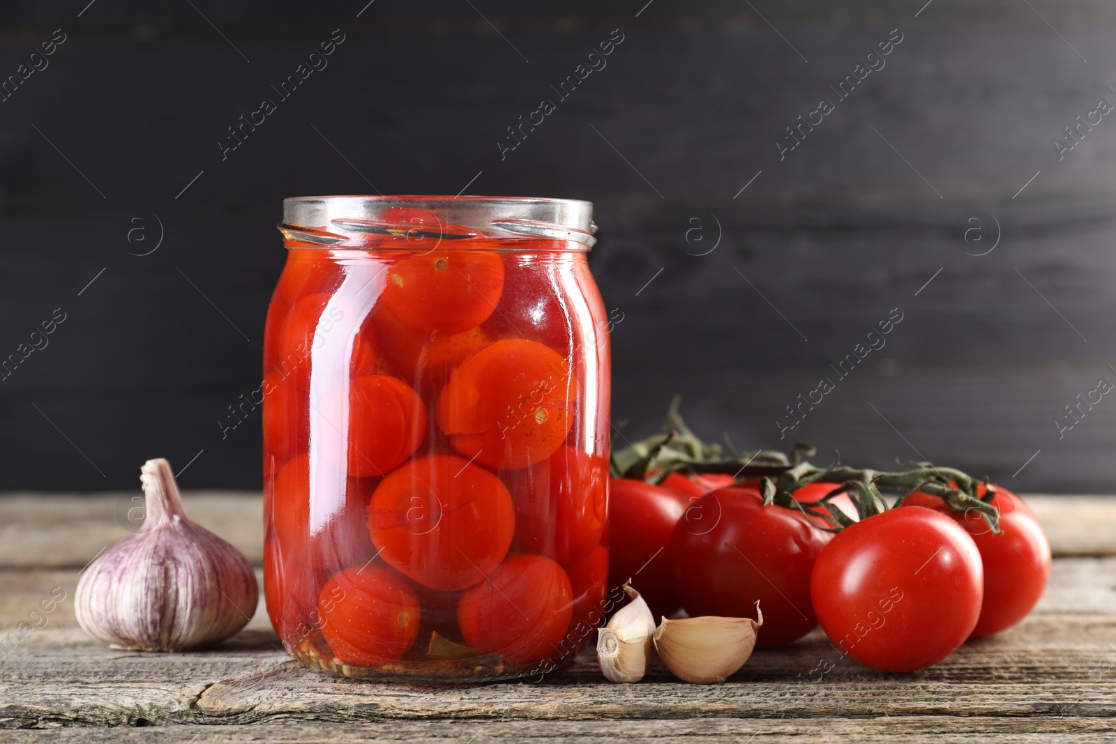 Photo of Tasty pickled tomatoes in jar, fresh vegetables and garlic on wooden table