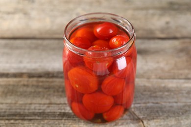 Tasty pickled tomatoes in jar on wooden table