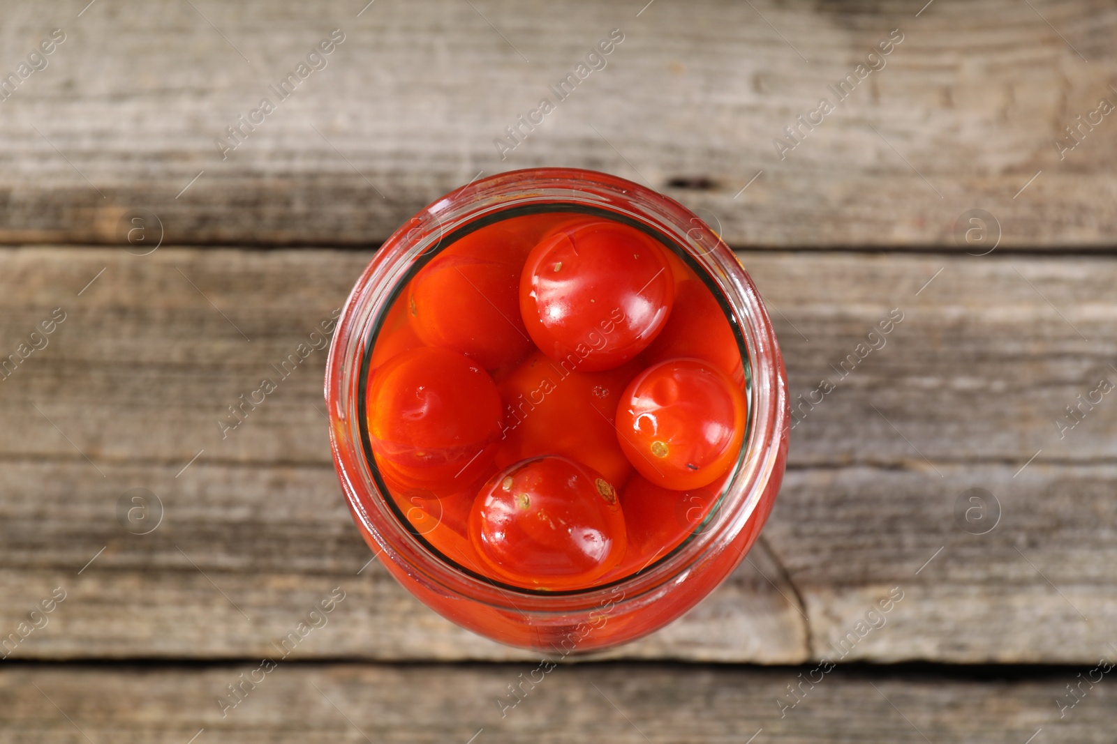 Photo of Tasty pickled tomatoes in jar on wooden table, top view