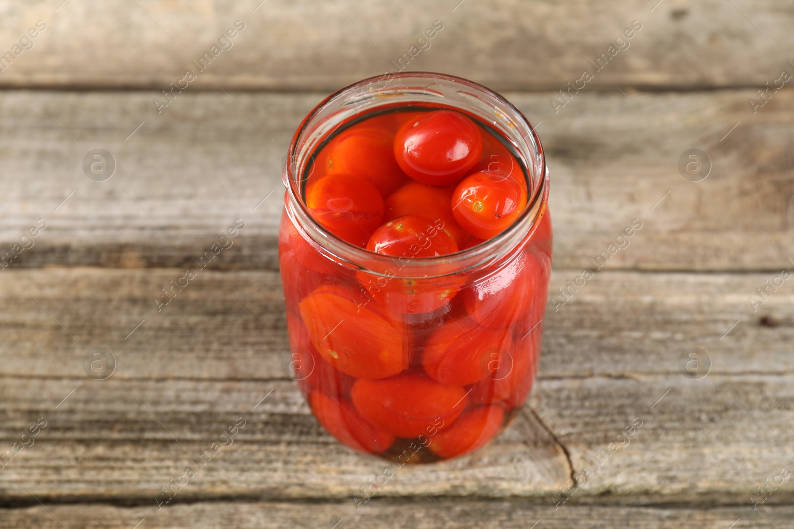 Photo of Tasty pickled tomatoes in jar on wooden table