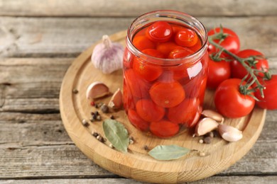 Tasty pickled tomatoes in jar, fresh vegetables and spices on wooden table