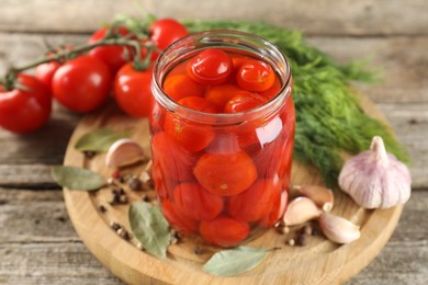 Tasty pickled tomatoes in jar, fresh vegetables and spices on wooden table