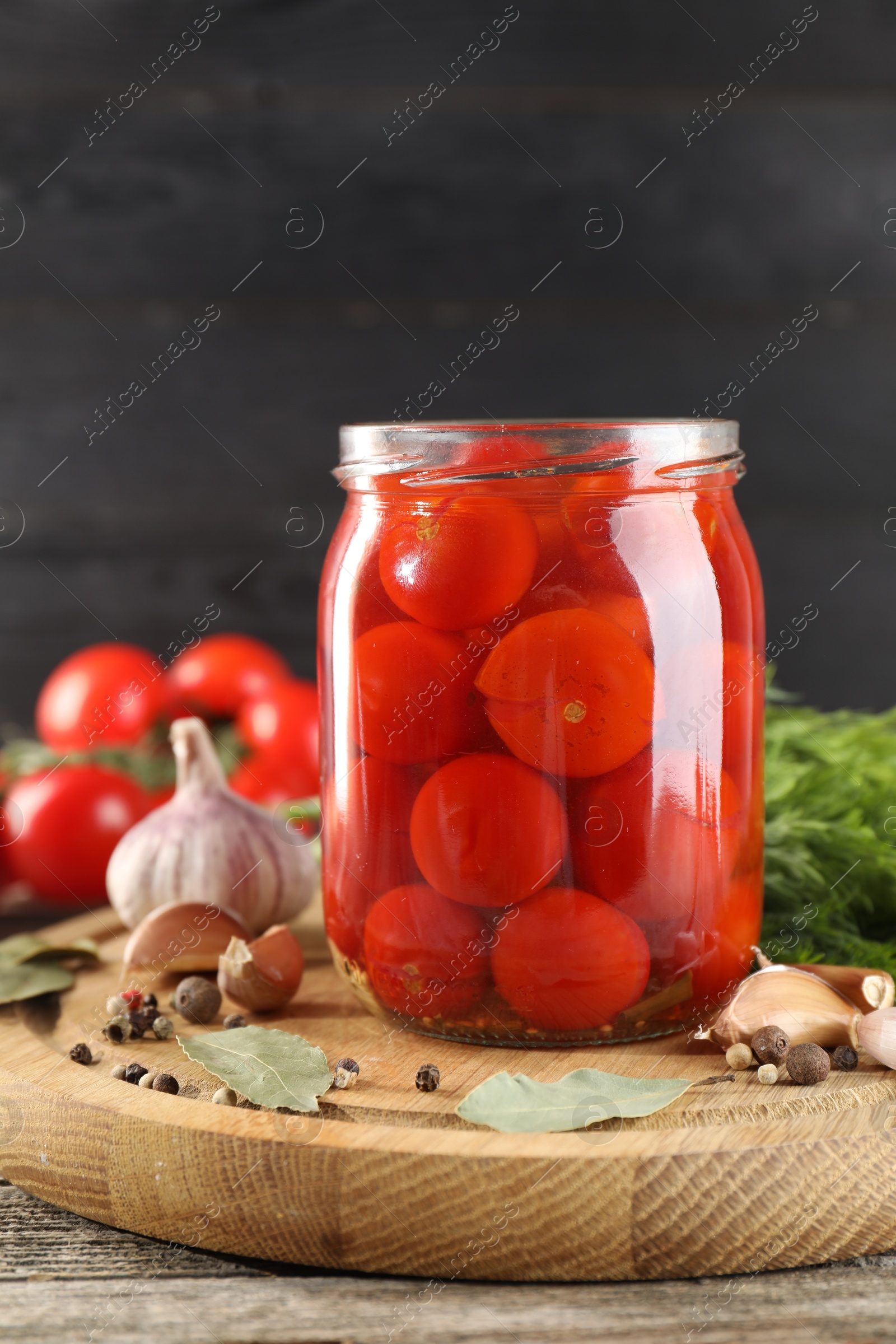 Photo of Tasty pickled tomatoes in jar and spices on wooden table