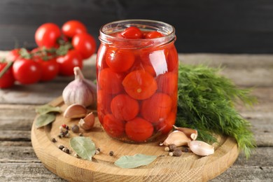 Tasty pickled tomatoes in jar and spices on wooden table