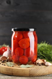 Photo of Tasty pickled tomatoes in jar and spices on wooden table