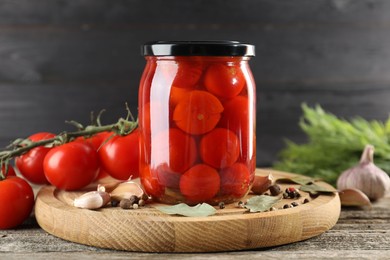 Tasty pickled tomatoes in jar, fresh vegetables and spices on wooden table